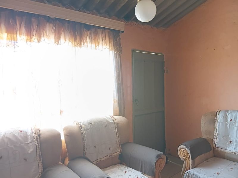 A living room area featuring a corrugated ceiling and a simple timber door, requiring cosmetic updates and wall repairs.
