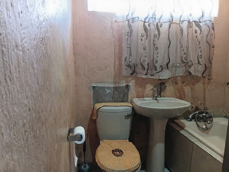 A dated bathroom featuring a pedestal basin, toilet, and bathtub, currently requiring significant wall repairs and cosmetic refurbishment to improve its condition.
