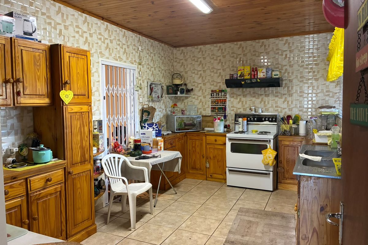 A dated kitchen featuring wooden cabinetry, tiled walls and flooring, and a timber ceiling, offering a functional layout with potential for modern renovation.