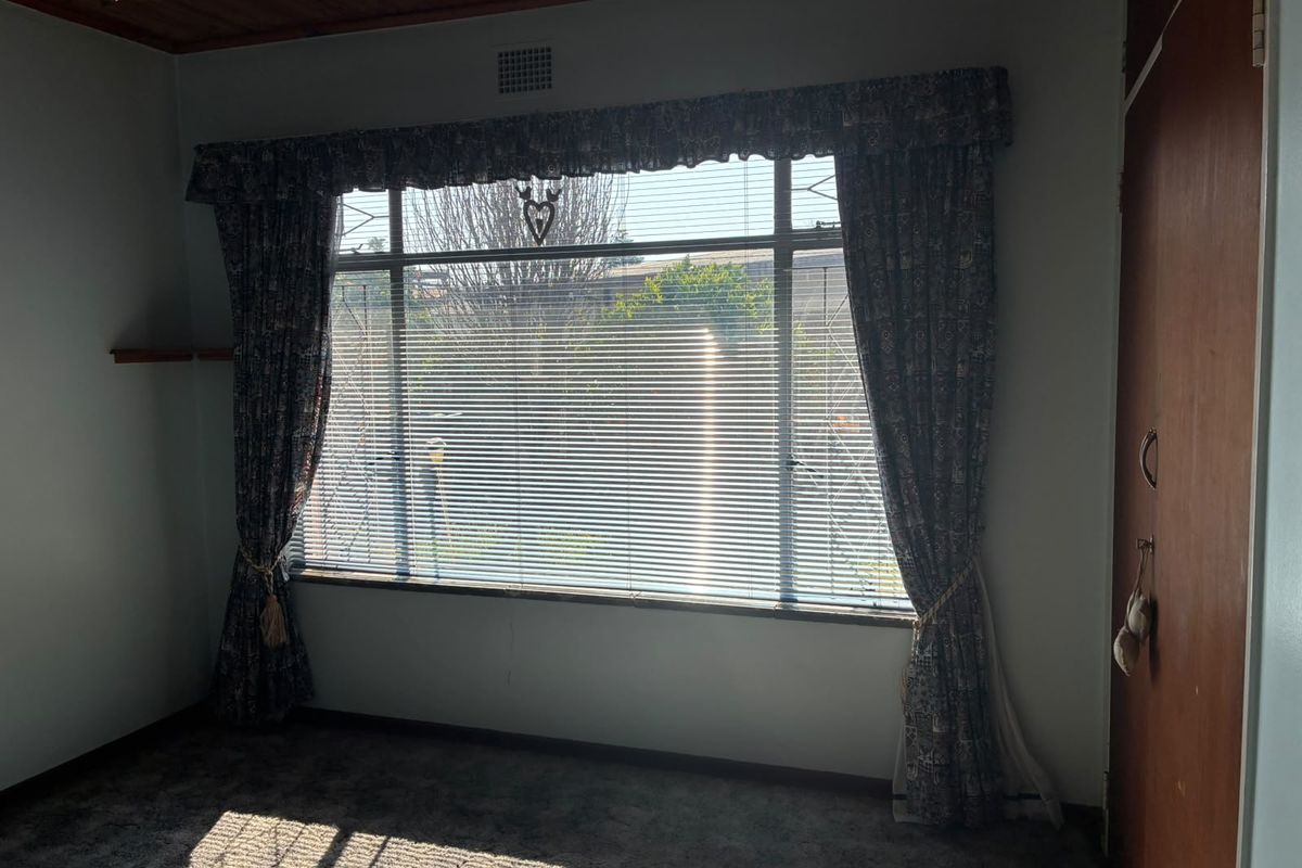 A vacant bedroom featuring a large window with security bars, built-in wardrobe, and timber ceiling, offering a blank canvas for renovation.