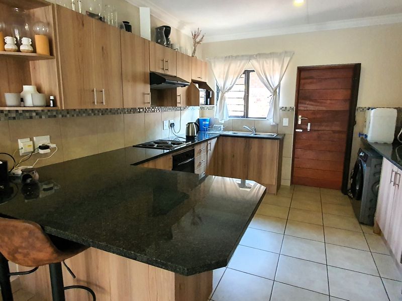 Functional kitchen featuring wood-finish cabinetry, granite countertops, built-in oven and hob, and tiled flooring with direct access to an exterior door.