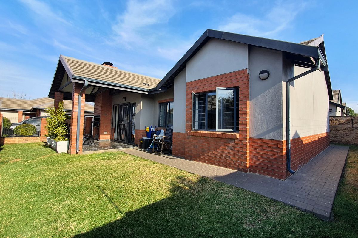 Rear view of the townhouse featuring a covered patio with a built-in braai, brick and plaster facade, and a well-maintained garden.