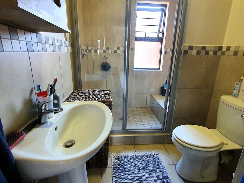 A functional bathroom featuring a pedestal basin, a glass-enclosed shower, and a standard toilet with neutral wall and floor tiling.