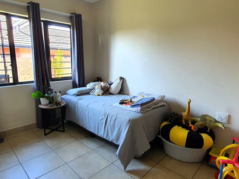 A functional bedroom featuring tiled flooring and windows fitted with security bars, providing a practical space for a child or guest.