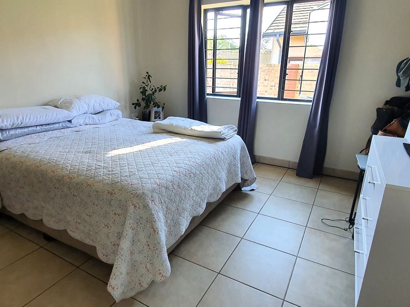 A functional bedroom featuring tiled flooring and windows fitted with security bars, providing a practical and well-lit living space.
