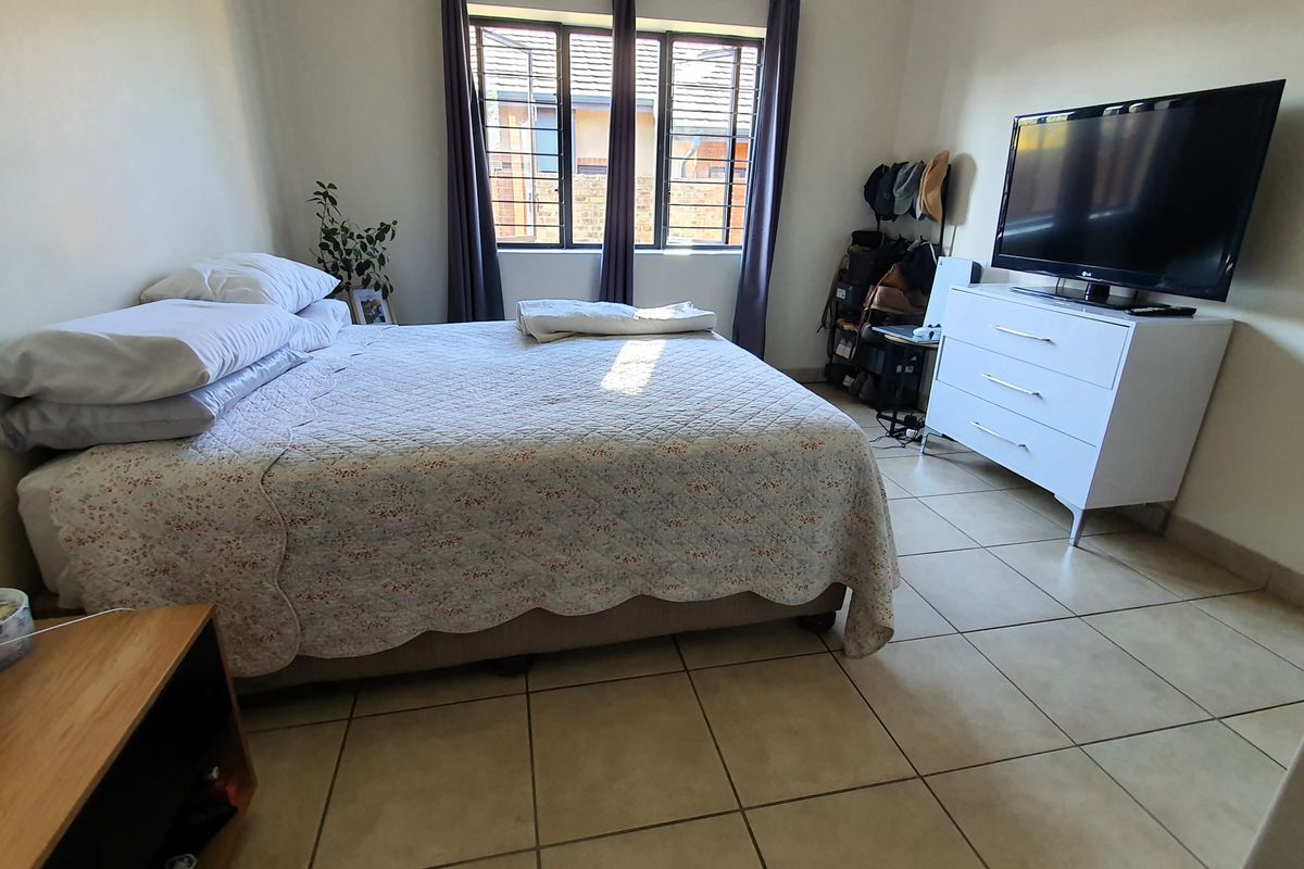 A functional bedroom featuring tiled flooring and windows fitted with security bars, providing a practical and secure living space.