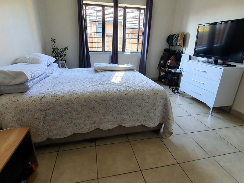A functional bedroom featuring tiled flooring and windows fitted with security bars, providing a practical and secure living space.