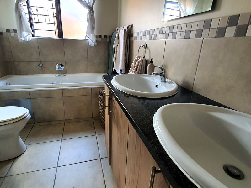A functional bathroom featuring a double vanity with granite countertop, a bathtub, and tiled finishes throughout.