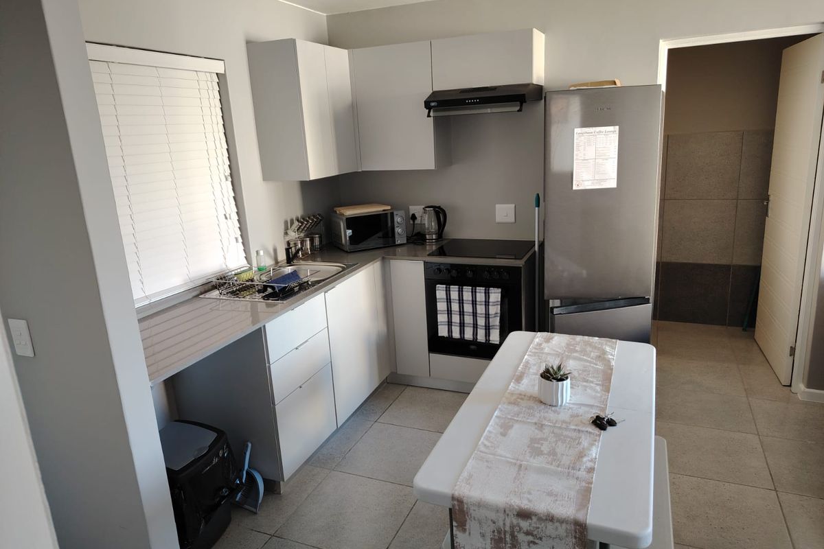 Modern kitchen featuring light grey cabinetry, stone countertops, integrated oven and hob, and tiled flooring, offering a clean and functional cooking space.