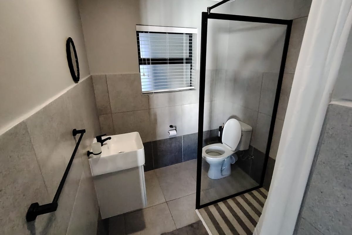 Modern bathroom featuring a vanity basin, toilet, and a walk-in shower with a sleek black-framed glass screen and neutral wall tiling.