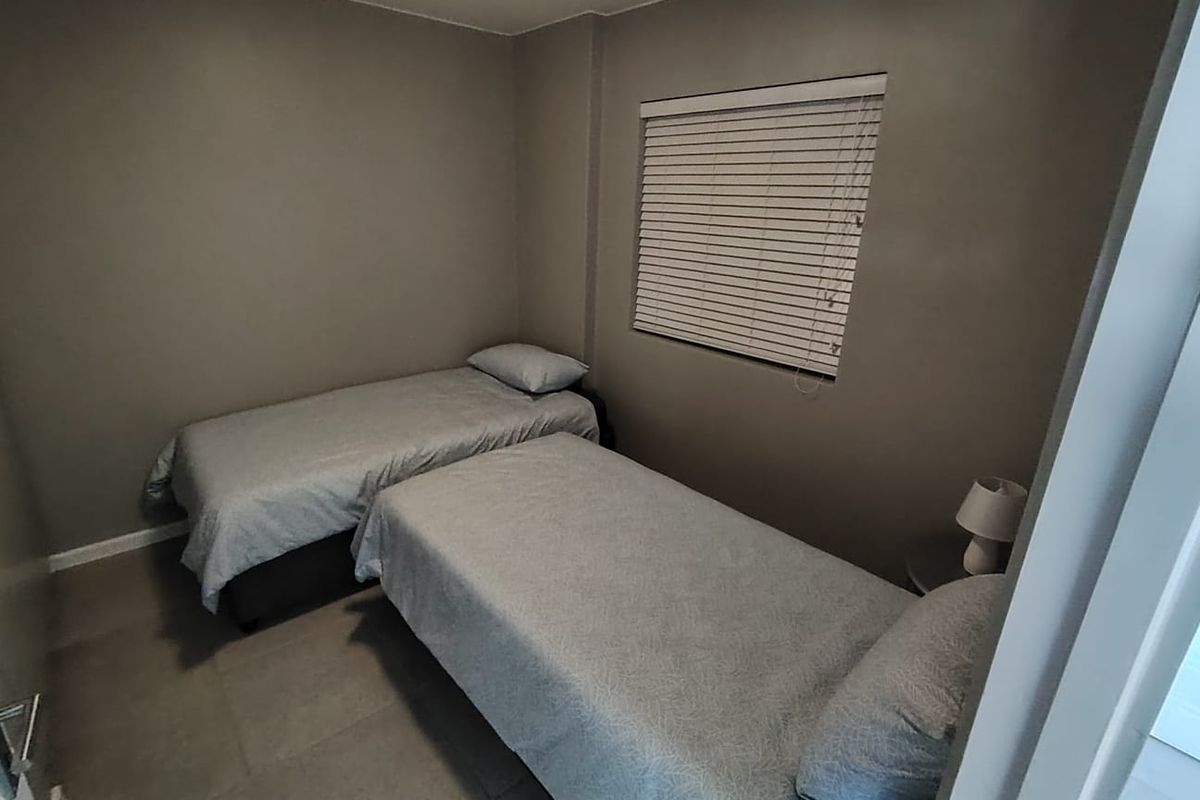 A compact bedroom featuring neutral wall tones, tiled flooring, and fitted venetian blinds, providing a functional and simple living space.
