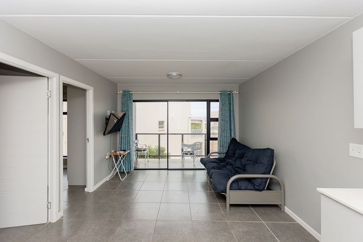 Open plan living area featuring neutral grey walls, tiled flooring, and a large sliding glass door providing access to the balcony.