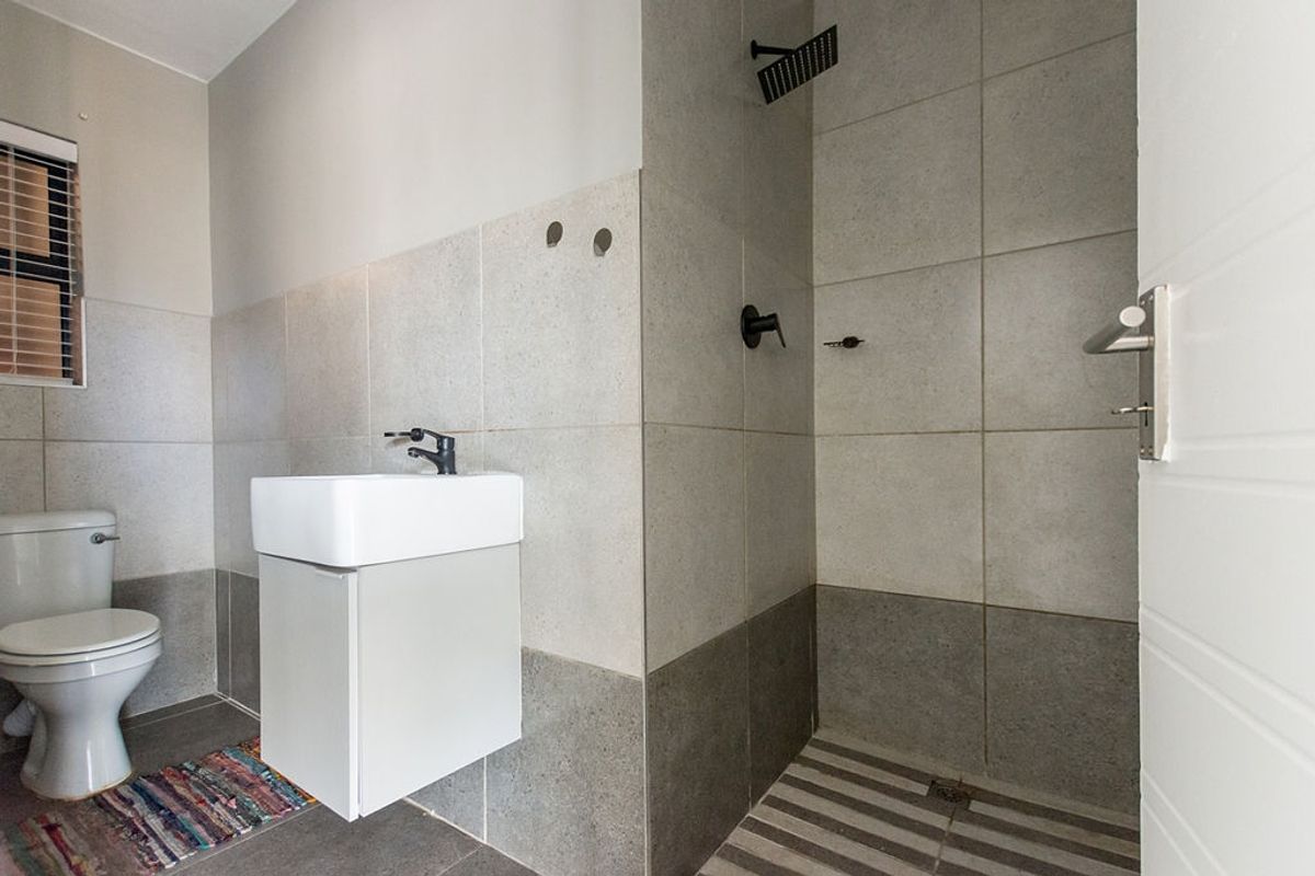 Modern bathroom featuring a walk-in shower with black fixtures, a wall-mounted vanity with basin, and neutral grey floor-to-ceiling tiling.
