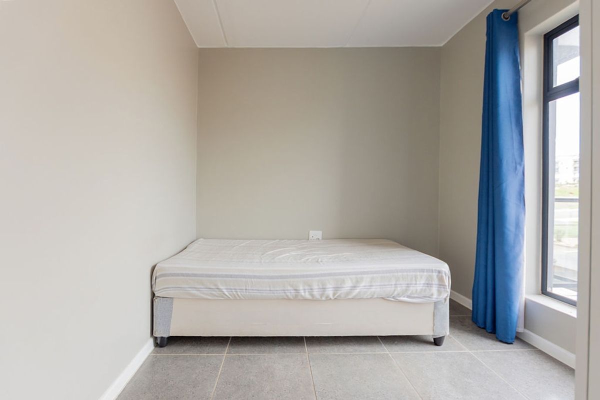 A simple, neutral-toned bedroom featuring tiled flooring and a large window that provides natural light.