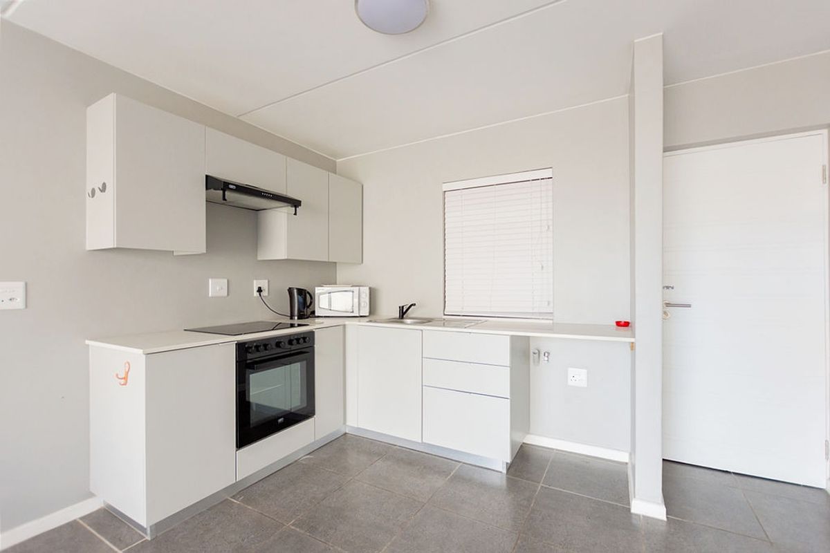 A clean, modern kitchen featuring white built-in cabinetry, an integrated oven and hob, extractor fan, and neutral tiled flooring.