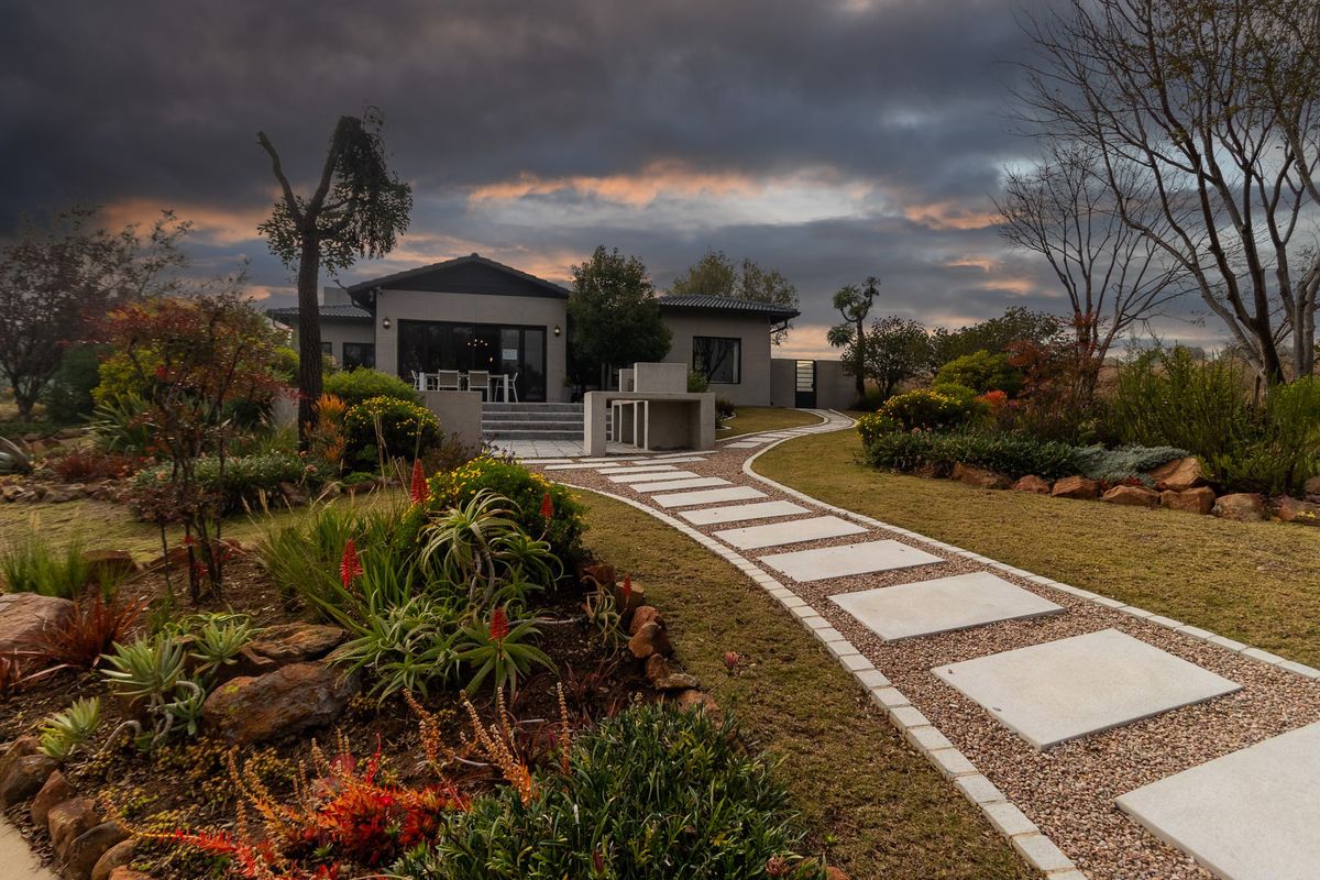 A beautifully landscaped rear garden featuring a stone paved walkway leading to a tiled patio with a built-in outdoor braai area.