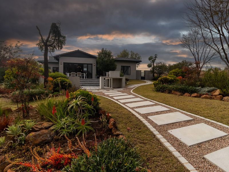 A beautifully landscaped rear garden featuring a stone paved walkway leading to a tiled patio with a built-in outdoor braai area.