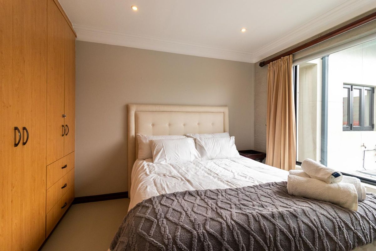 A well-maintained bedroom featuring a built-in wooden wardrobe, recessed downlighting, and a large window allowing for natural light.