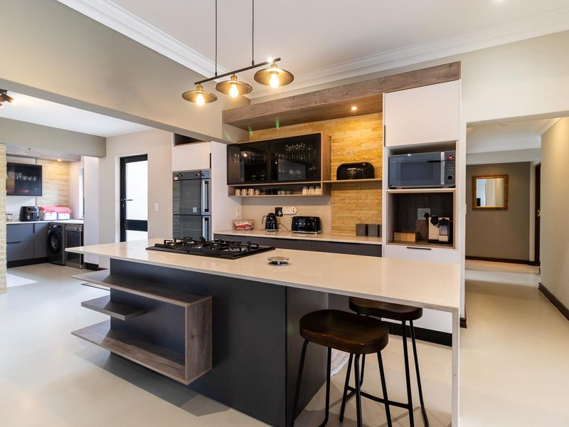 Modern kitchen featuring a large island with gas cooktop, stone countertops, stone feature wall, and integrated cabinetry with high-end finishes.