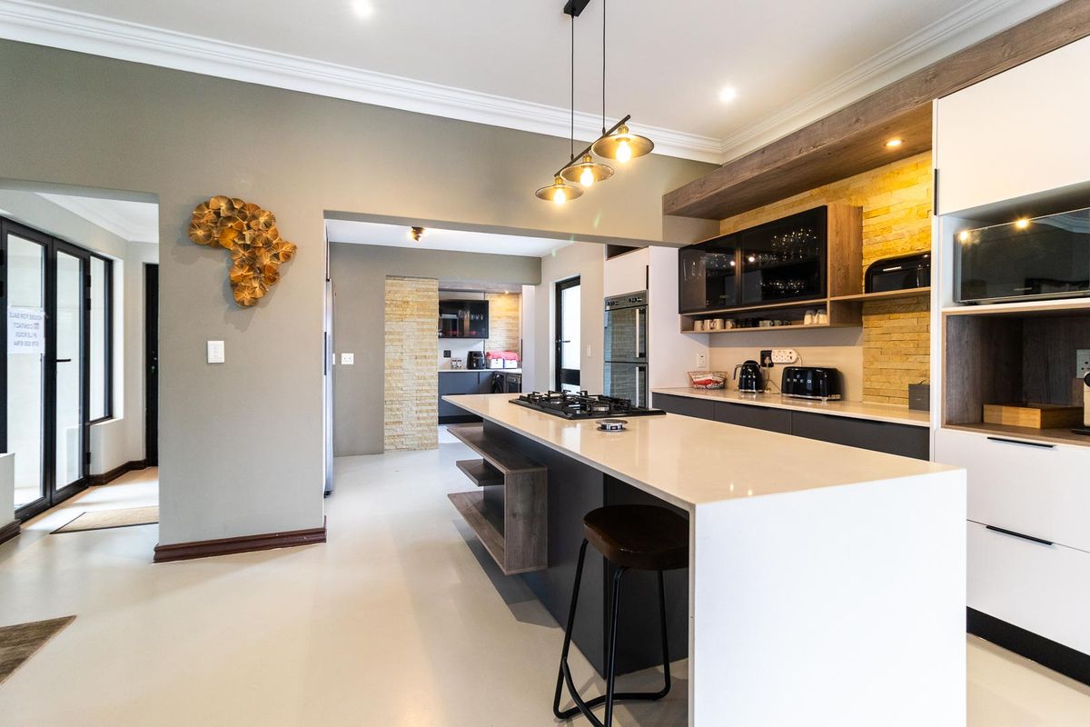 Modern kitchen featuring a large island with gas hob, stone countertops, sleek cabinetry, and stylish pendant lighting, flowing into an adjacent scullery area.