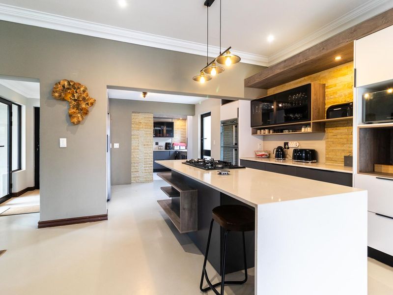 Modern kitchen featuring a large island with gas hob, stone countertops, sleek cabinetry, and stylish pendant lighting, flowing into an adjacent scullery area.