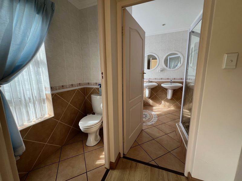 A functional bathroom featuring dual pedestal sinks, a separate toilet area, and a shower enclosure with tiled finishes throughout.