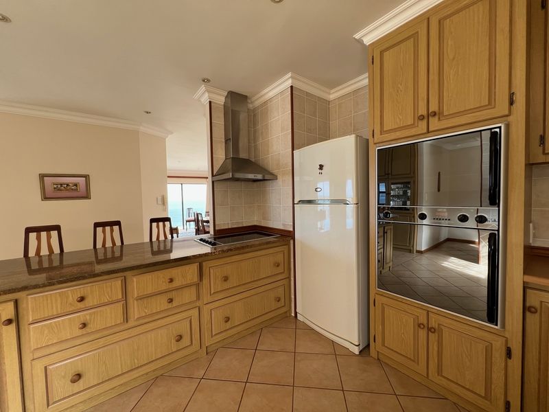 A functional kitchen featuring wooden cabinetry, granite countertops, a built-in oven, and a stainless steel extractor fan, with tiled flooring and backsplash.