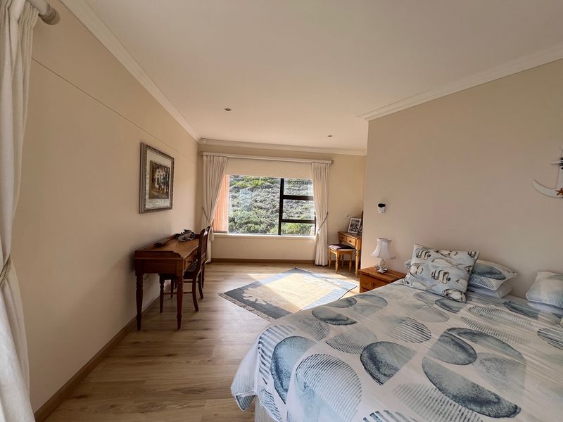 A well-maintained bedroom featuring light-toned laminate flooring, neutral wall finishes, and a large window providing natural light and garden views.