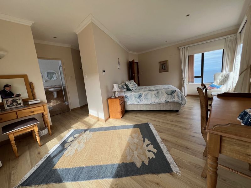 Spacious bedroom featuring light laminate flooring, recessed lighting, and an adjoining en-suite bathroom with ocean views.