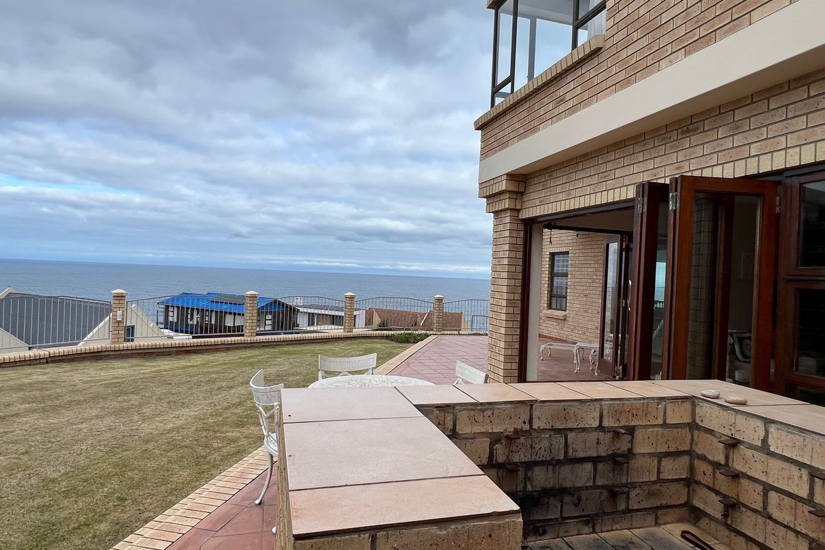 Rear exterior view featuring a brick facade, tiled patio with a built-in braai, and ocean views.
