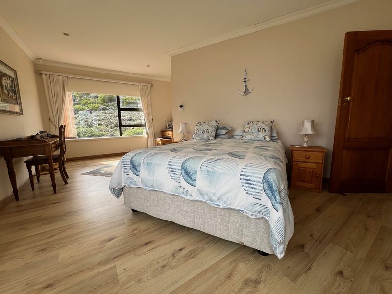 A well-maintained bedroom featuring light-toned laminate flooring, neutral walls, and a large window providing natural light and garden views.
