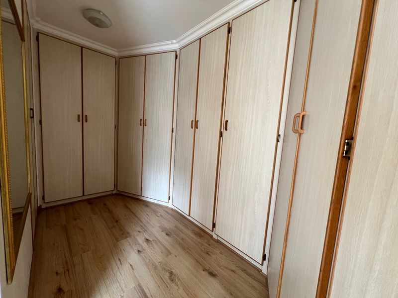 A clean, empty bedroom featuring extensive built-in wooden cupboards and modern laminate flooring, offering ample storage space.