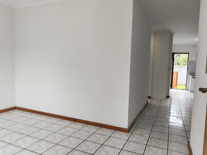 An empty, neutral-toned living area featuring ceramic tile flooring and timber skirting, with a clear view through to the rear entrance.