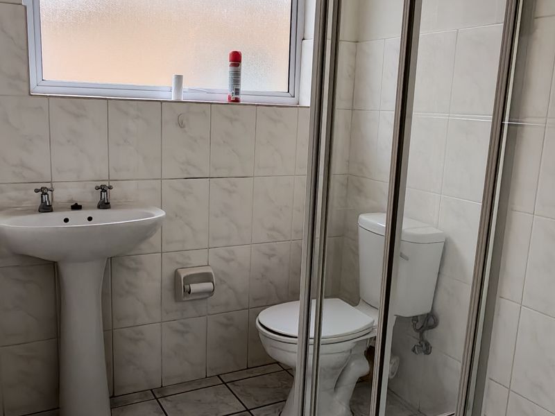A functional bathroom featuring a pedestal basin, toilet, and a glass-enclosed shower with tiled walls and flooring throughout.