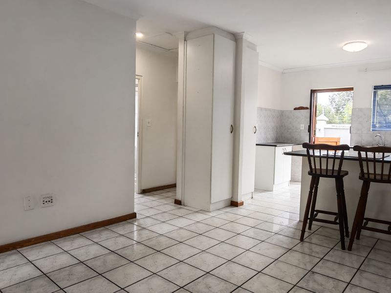 An open-plan kitchen and dining area featuring tiled flooring, a breakfast bar, and built-in cabinetry with neutral finishes.