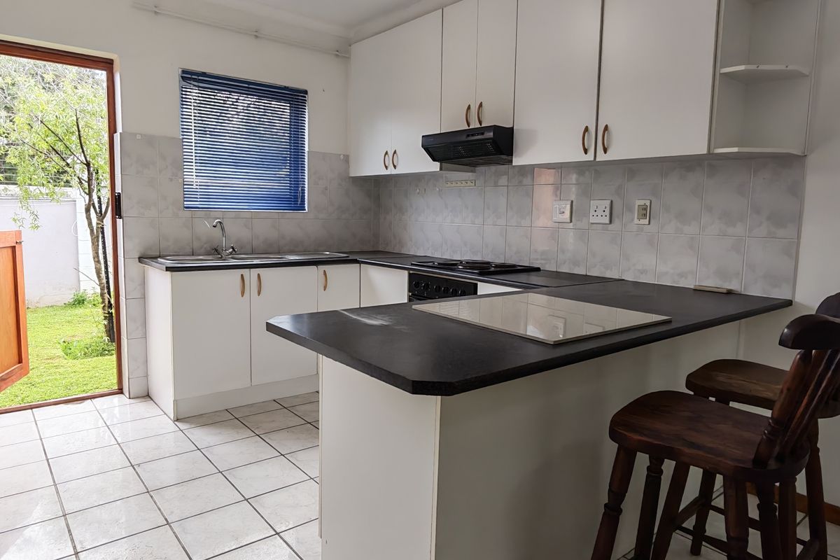 A functional kitchen featuring white cabinetry, dark laminate countertops, a built-in hob with extractor, and direct access to the rear garden.