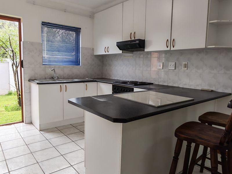 A functional kitchen featuring white cabinetry, dark laminate countertops, a built-in hob with extractor, and direct access to the rear garden.