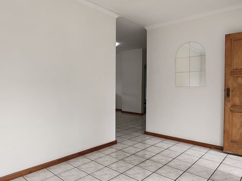 A vacant hallway featuring neutral white walls, tiled flooring, and a traditional wooden door, providing a clean and simple transition between living spaces.
