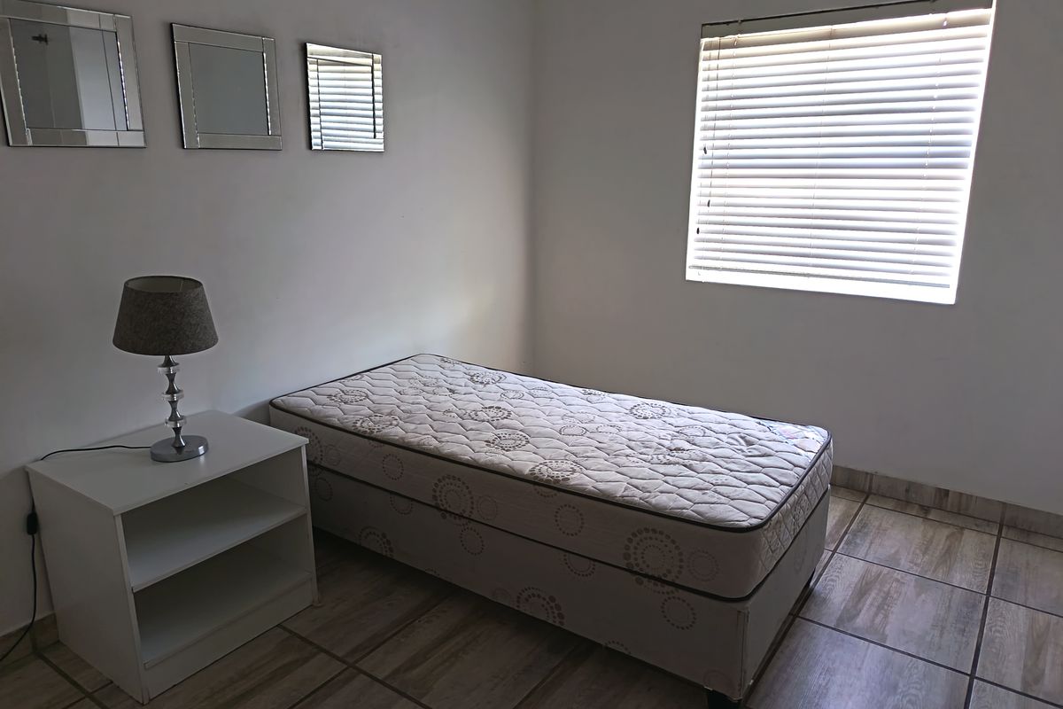 A simple bedroom featuring tiled flooring and venetian blinds, providing a functional and neutral space.