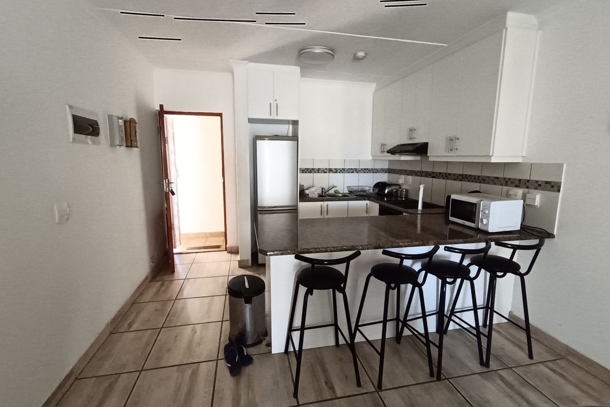 Compact kitchen featuring white cabinetry, granite countertops, a breakfast bar, and tiled flooring, providing a functional and efficient cooking and dining space.