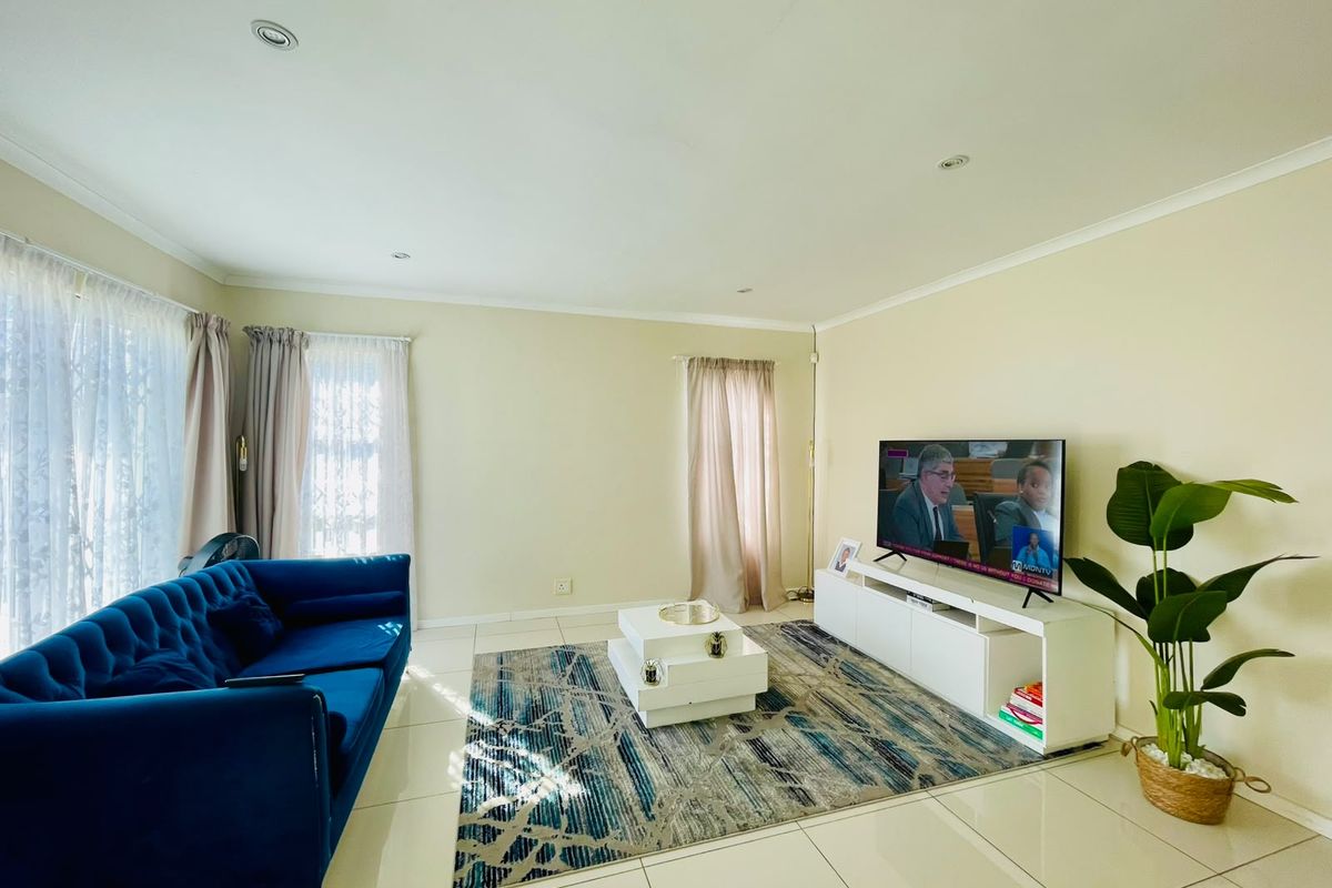 A bright and spacious living room featuring neutral tiled flooring, recessed downlighting, and large windows with curtain tracks.