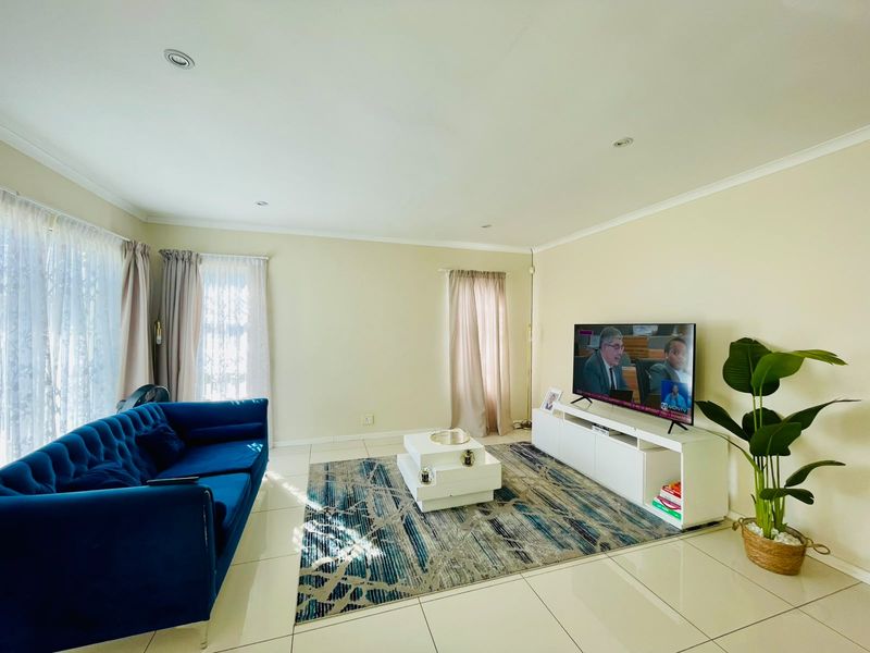 A bright and spacious living room featuring neutral tiled flooring, recessed downlighting, and large windows with curtain tracks.