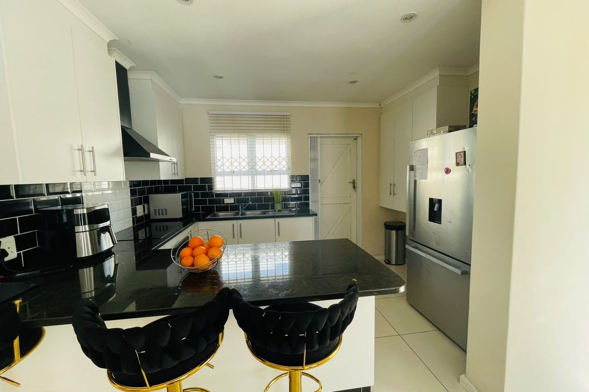 Modern kitchen featuring sleek black granite countertops, white cabinetry, subway tile backsplash, and a breakfast bar island with integrated appliances.