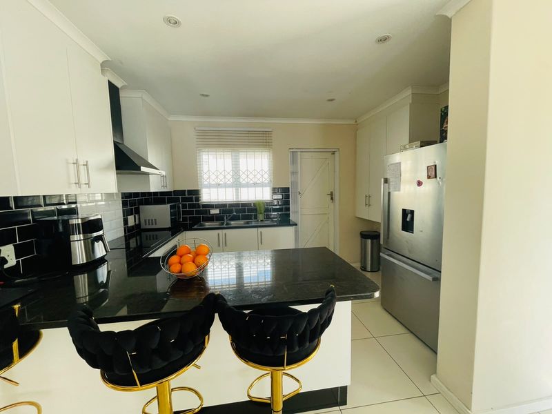 Modern kitchen featuring sleek black granite countertops, white cabinetry, subway tile backsplash, and a breakfast bar island with integrated appliances.