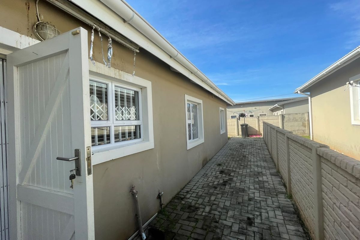 A side exterior view of the townhouse featuring a paved walkway, boundary wall, and external utility access points.