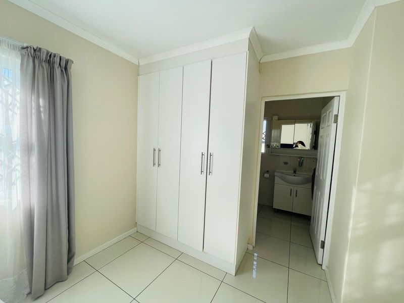 A clean, neutral bedroom featuring built-in cupboards, tiled flooring, and direct access to an en-suite bathroom.