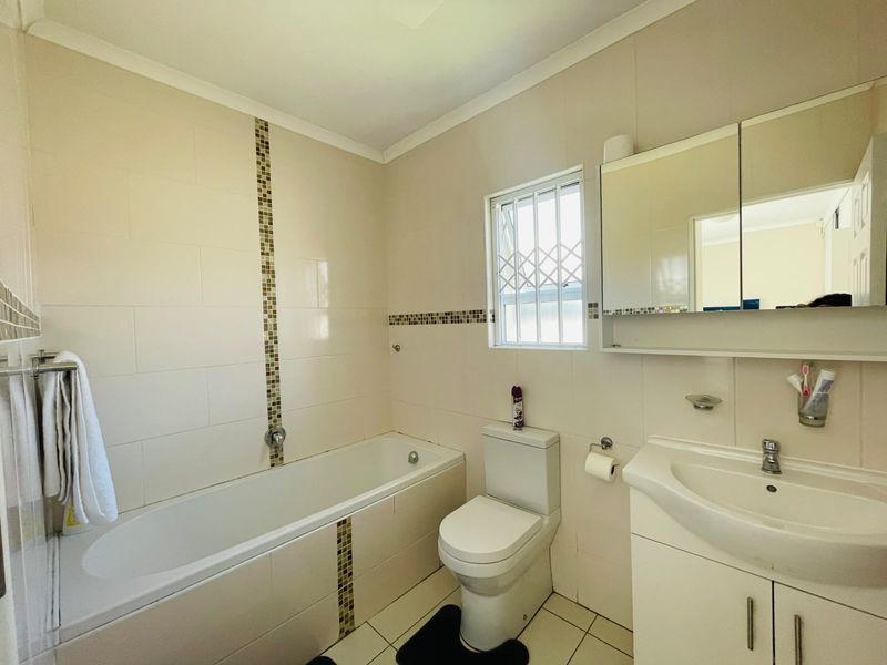 A functional bathroom featuring a bathtub, toilet, and vanity cabinet with a mirror, finished with neutral wall and floor tiles.