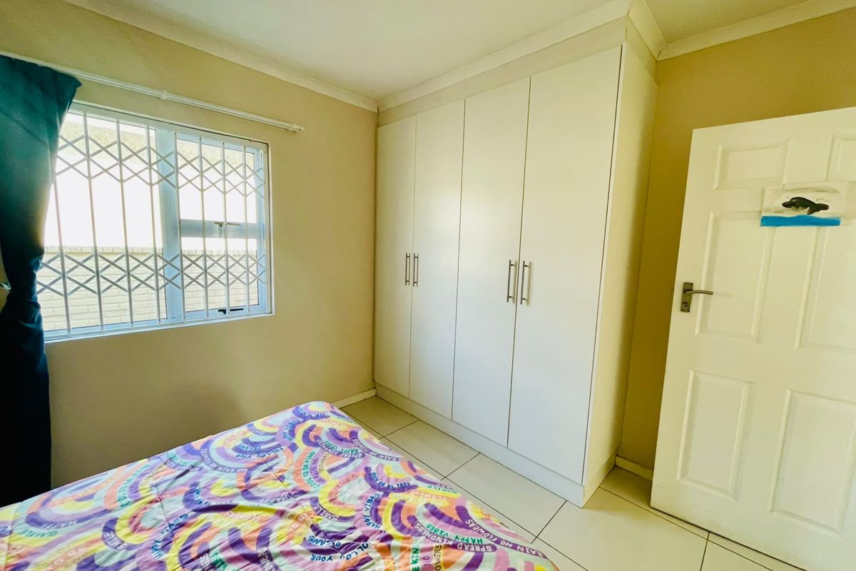 A bedroom featuring built-in wardrobes, tiled flooring, and a window fitted with a security gate.