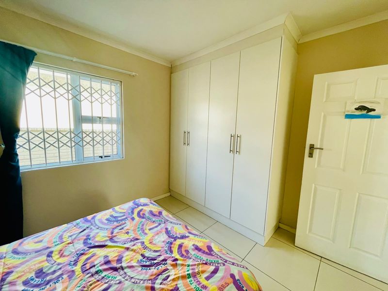 A bedroom featuring built-in wardrobes, tiled flooring, and a window fitted with a security gate.