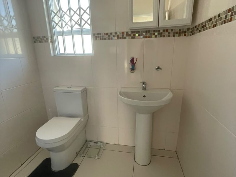 A functional bathroom featuring a pedestal basin, toilet, and wall-mounted medicine cabinet with tiled finishes throughout.